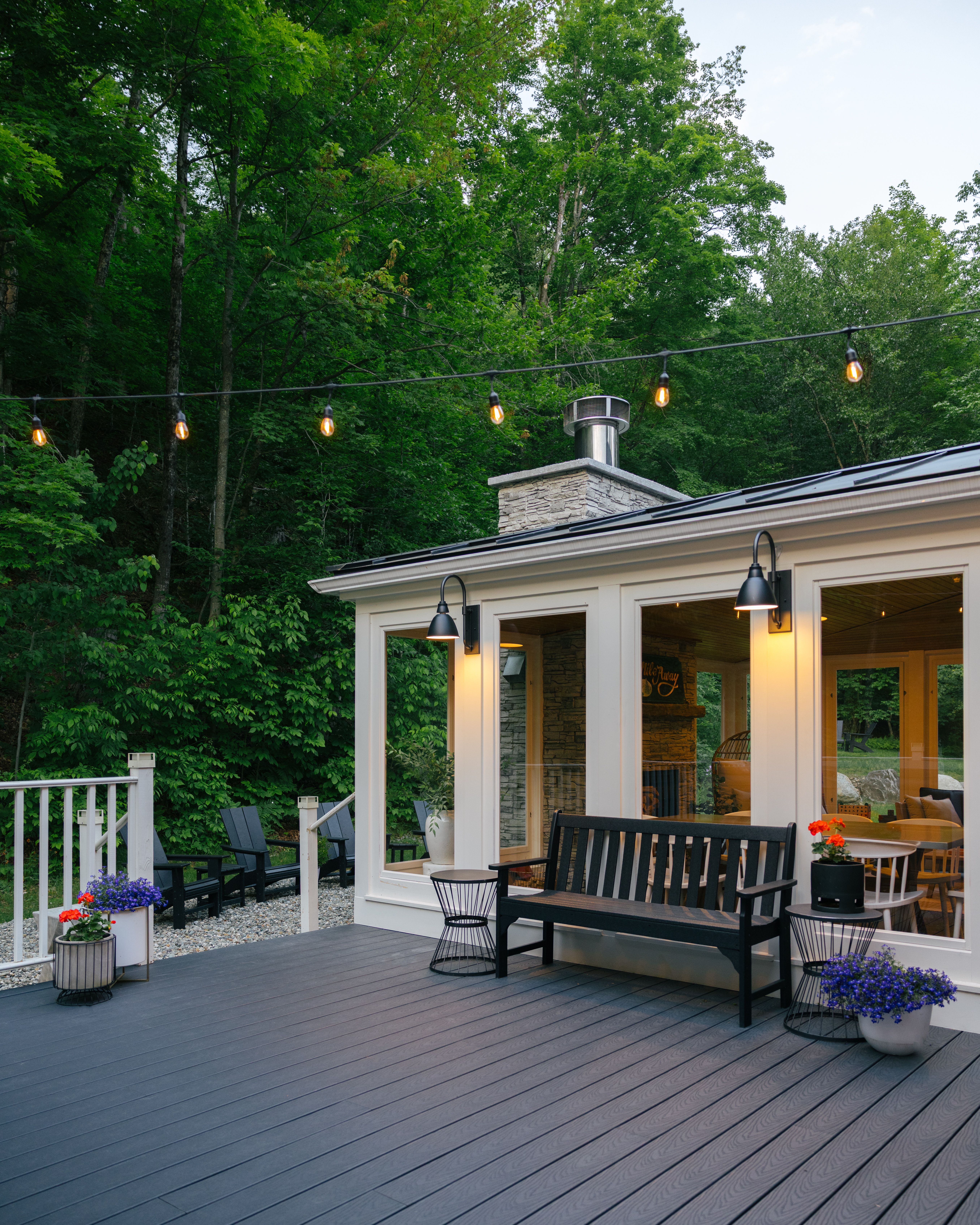 Covered outdoor seating area with bench and chairs overlooking the wooded yard